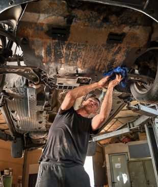 Repairman, worker repairing car, holding rag, wiping. Strong, hardworking man working in servicing center, mainteining automobiles. Concept of manual labor.