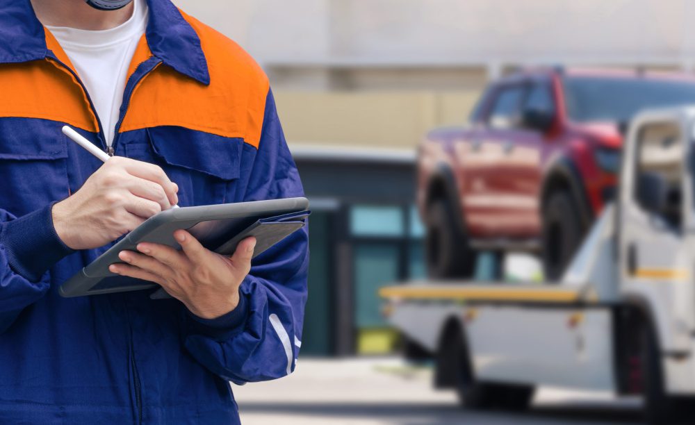Close up of insurance officer using electronic pen to recording data of broken pickup car on tablet while prepare for transporting to garage after accident on the road